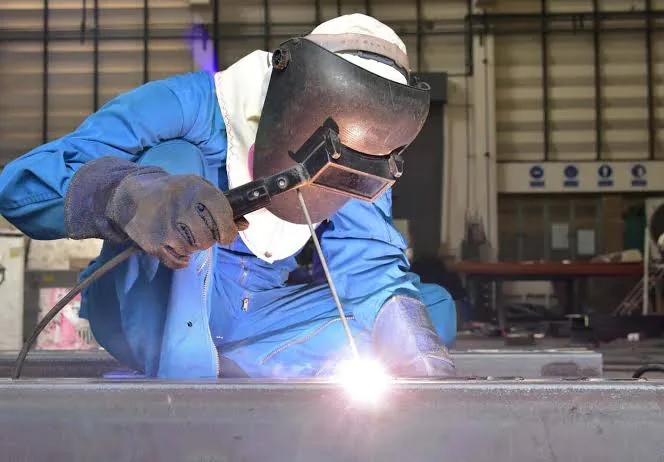 Apprenant du CFIS Mbour en tenue de soudure, masque et gants, soudant une pièce métallique